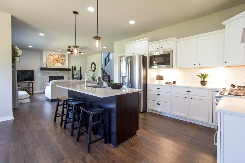 Transitional l-shaped laminate floor and brown floor eat-in kitchen photo with an undermount sink, recessed-panel cabinets, white cabinets, quartz countertops, white backsplash, subway tile backsplash, stainless steel appliances, an island and white countertops