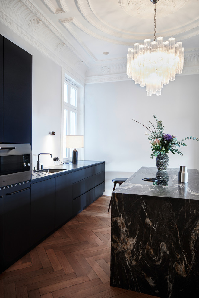 Mid-sized contemporary galley kitchen in Hamburg with an undermount sink, flat-panel cabinets, black cabinets, panelled appliances, with island, brown floor and black benchtop.