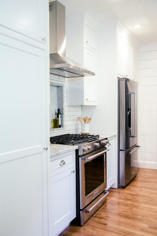 Mid-sized country galley eat-in kitchen in Austin with a farmhouse sink, white cabinets, white splashback, subway tile splashback, stainless steel appliances, medium hardwood floors, brown floor, quartzite benchtops, shaker cabinets and no island.