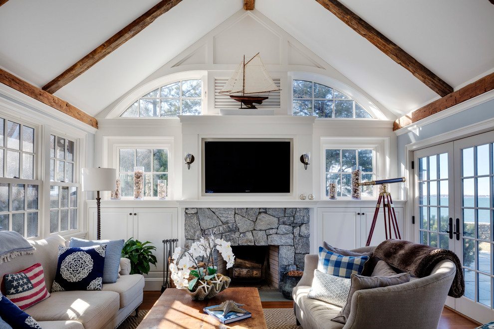 This is an example of a beach style family room in Boston with white walls, medium hardwood floors, a standard fireplace, a stone fireplace surround and brown floor.