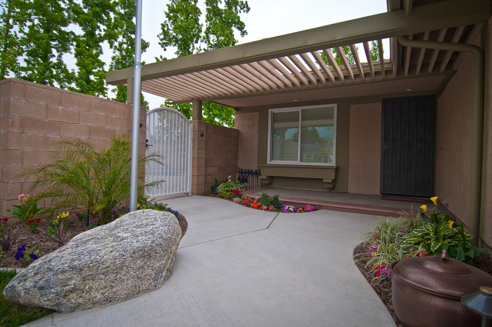 This is an example of a mid-sized tropical front yard verandah in Los Angeles with concrete slab and a pergola.