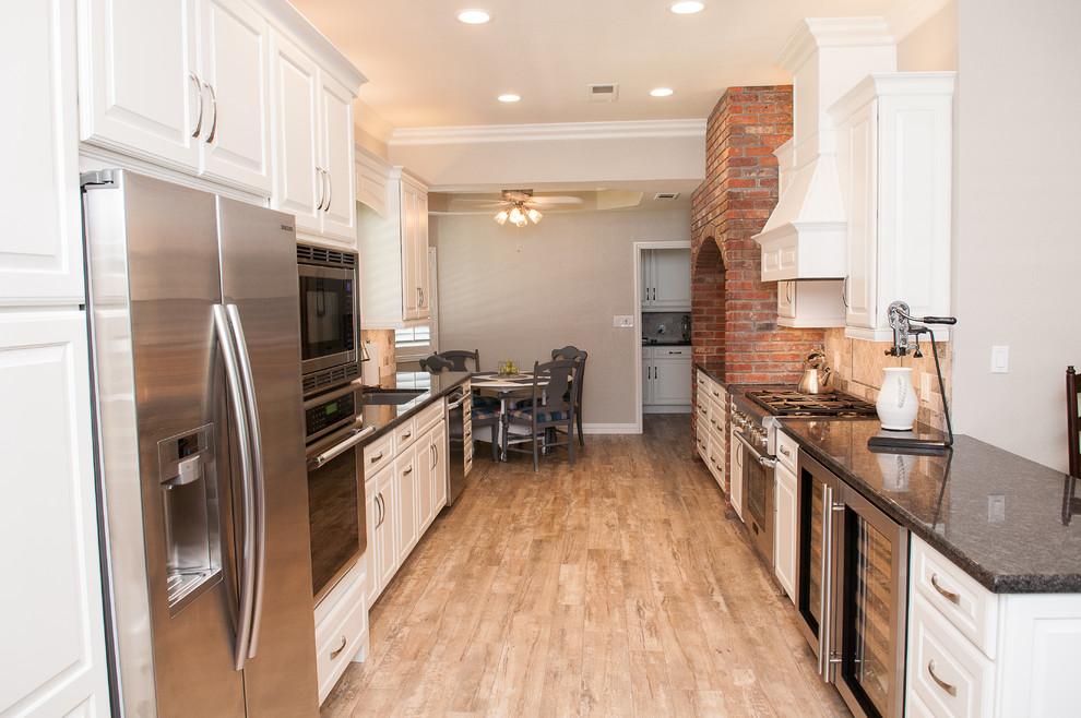 Mid-sized transitional galley porcelain tile and beige floor enclosed kitchen photo with a triple-bowl sink, raised-panel cabinets, white cabinets, granite countertops, beige backsplash, porcelain backsplash, stainless steel appliances and a peninsula