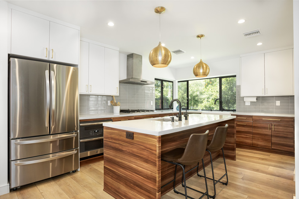 Inspiration for a mid-sized modern l-shaped open plan kitchen in Los Angeles with a farmhouse sink, flat-panel cabinets, medium wood cabinets, quartz benchtops, grey splashback, subway tile splashback, stainless steel appliances, laminate floors, with island, yellow floor and white benchtop.