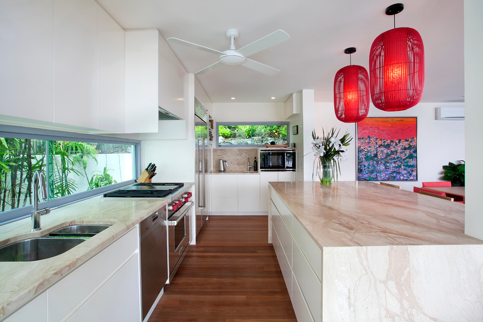 Design ideas for an expansive beach style galley open plan kitchen in Sunshine Coast with a double-bowl sink, flat-panel cabinets, white cabinets, marble benchtops, glass sheet splashback, stainless steel appliances, medium hardwood floors and with island.