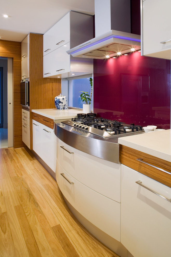 Asian open plan kitchen in Perth with an undermount sink, flat-panel cabinets, white cabinets, granite benchtops, white splashback, glass sheet splashback, stainless steel appliances, light hardwood floors and with island.
