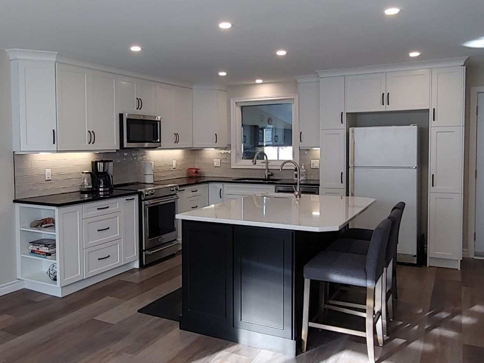 Example of a mid-sized transitional l-shaped medium tone wood floor and gray floor kitchen pantry design in Toronto with an undermount sink, shaker cabinets, white cabinets, quartzite countertops, gray backsplash, subway tile backsplash, stainless steel appliances, an island and black countertops