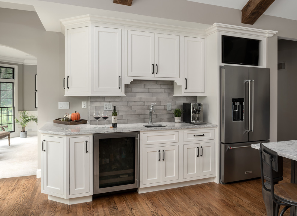 Photo of a large transitional l-shaped eat-in kitchen in St Louis with an undermount sink, flat-panel cabinets, white cabinets, quartz benchtops, grey splashback, ceramic splashback, stainless steel appliances, medium hardwood floors, with island, brown floor and white benchtop.
