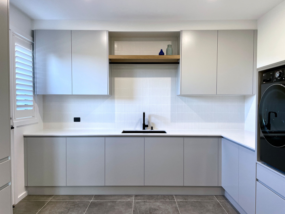 Photo of an expansive modern u-shaped dedicated laundry room in Sydney with an undermount sink, flat-panel cabinets, grey cabinets, quartz benchtops, white splashback, ceramic splashback, white walls, ceramic floors, a side-by-side washer and dryer, grey floor and white benchtop.