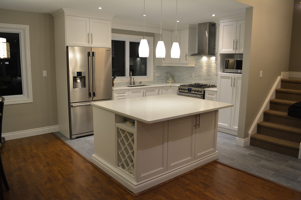 Inspiration for a mid-sized transitional l-shaped porcelain tile eat-in kitchen remodel in Toronto with an undermount sink, white cabinets, quartzite countertops, stainless steel appliances, an island, shaker cabinets, gray backsplash and matchstick tile backsplash