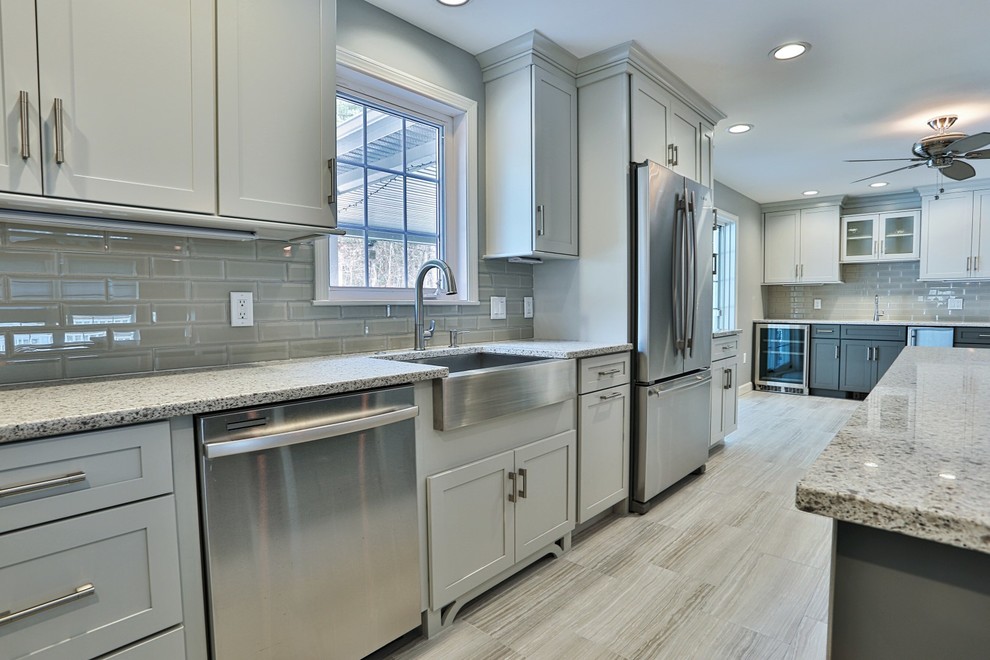 Photo of a large transitional l-shaped open plan kitchen in Boston with a farmhouse sink, shaker cabinets, white cabinets, granite benchtops, grey splashback, subway tile splashback, stainless steel appliances, porcelain floors, with island and beige floor.