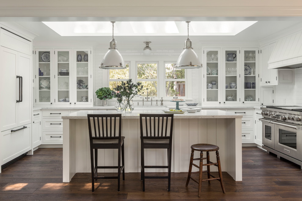 Design ideas for a large country u-shaped open plan kitchen in San Francisco with a farmhouse sink, white cabinets, white splashback, subway tile splashback, stainless steel appliances, dark hardwood floors, with island and glass-front cabinets.