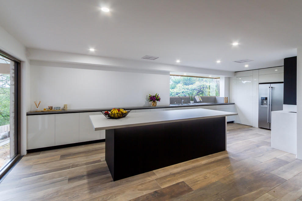 Expansive modern u-shaped eat-in kitchen in Melbourne with a double-bowl sink, flat-panel cabinets, black cabinets, quartz benchtops, white splashback, window splashback, stainless steel appliances, porcelain floors, with island, brown floor and white benchtop.