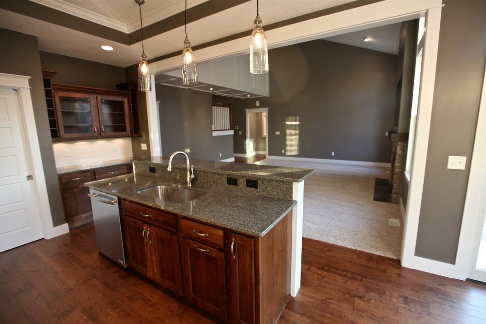 Inspiration for a mid-sized l-shaped medium tone wood floor kitchen remodel in Chicago with an undermount sink, shaker cabinets, medium tone wood cabinets, granite countertops, white backsplash, ceramic backsplash, stainless steel appliances and an island