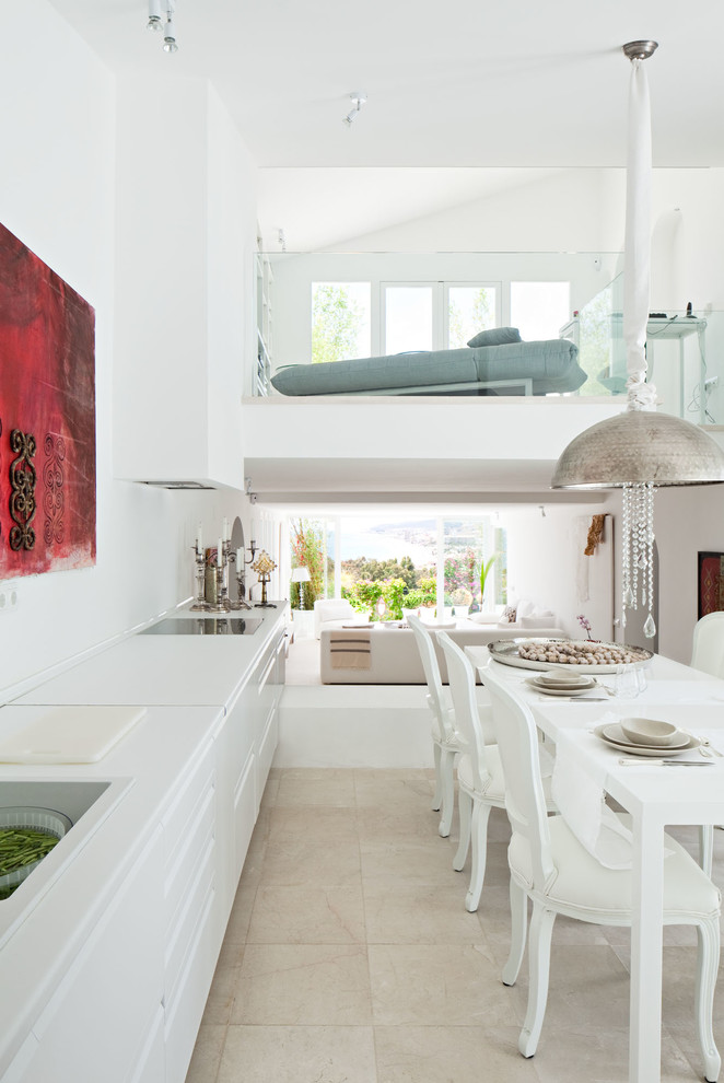 This is an example of a large contemporary single-wall eat-in kitchen in Malaga with a drop-in sink, flat-panel cabinets, white cabinets, solid surface benchtops, white splashback, white appliances, travertine floors, no island and white benchtop.