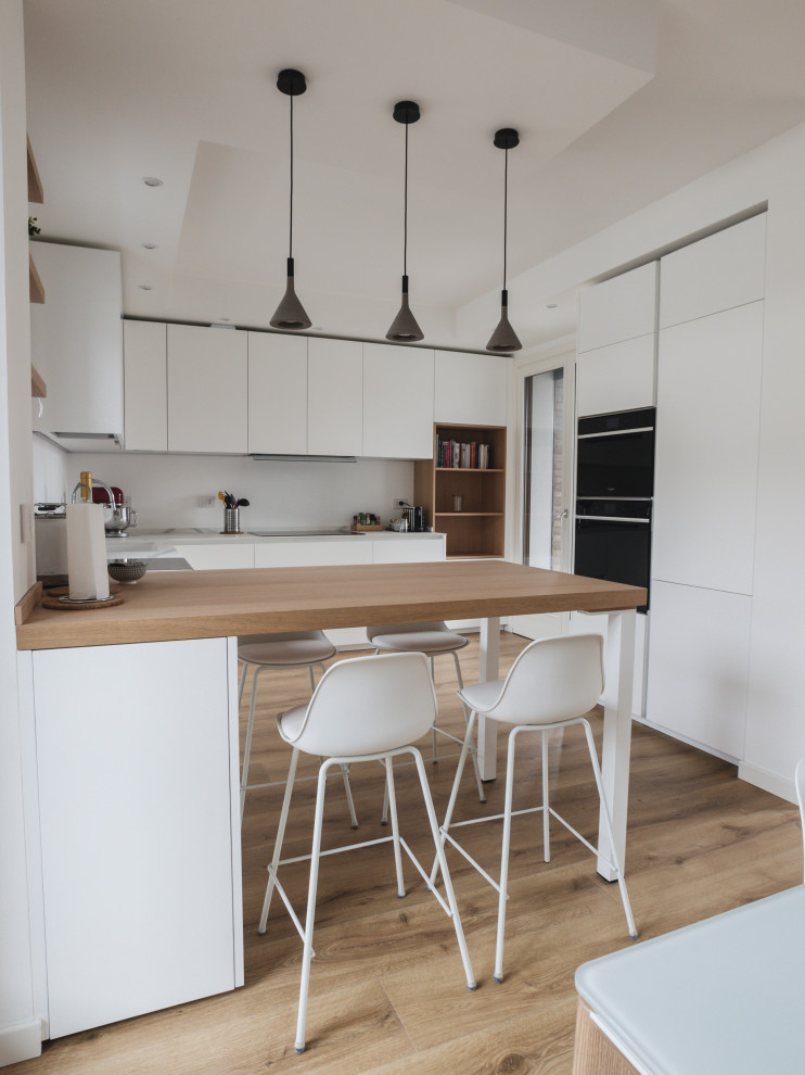 Design ideas for a mid-sized contemporary u-shaped open plan kitchen in Milan with a drop-in sink, flat-panel cabinets, white cabinets, quartz benchtops, black appliances, laminate floors, with island and white benchtop.