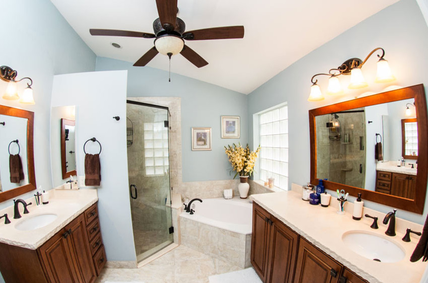 Example of a mid-sized transitional master beige tile and ceramic tile drop-in bathtub design in Miami with raised-panel cabinets, medium tone wood cabinets, blue walls, an undermount sink and solid surface countertops