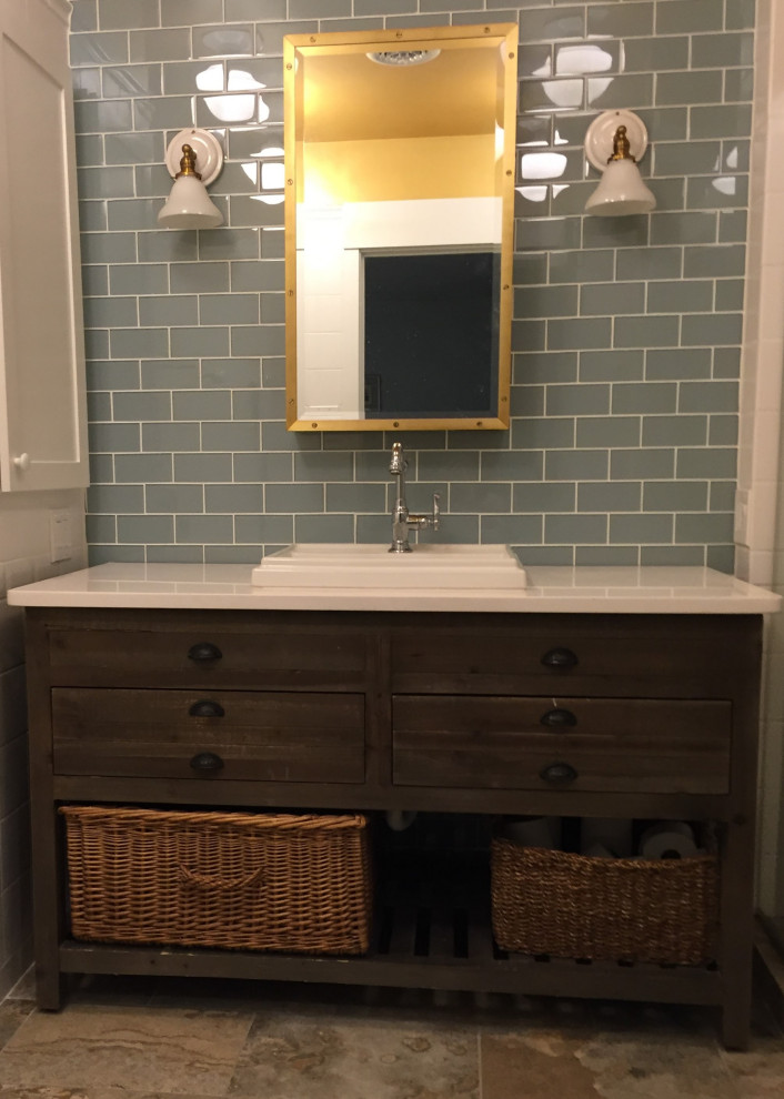 This is an example of a mid-sized industrial master bathroom in New York with furniture-like cabinets, distressed cabinets, an alcove tub, an alcove shower, a two-piece toilet, blue tile, glass sheet wall, white walls, porcelain floors, a drop-in sink, engineered quartz benchtops, multi-coloured floor, a hinged shower door and white benchtops.