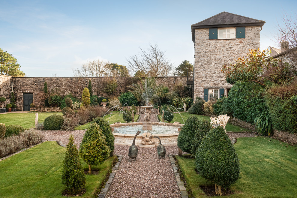 Traditional full sun garden in Other with a water feature, gravel and a stone fence.