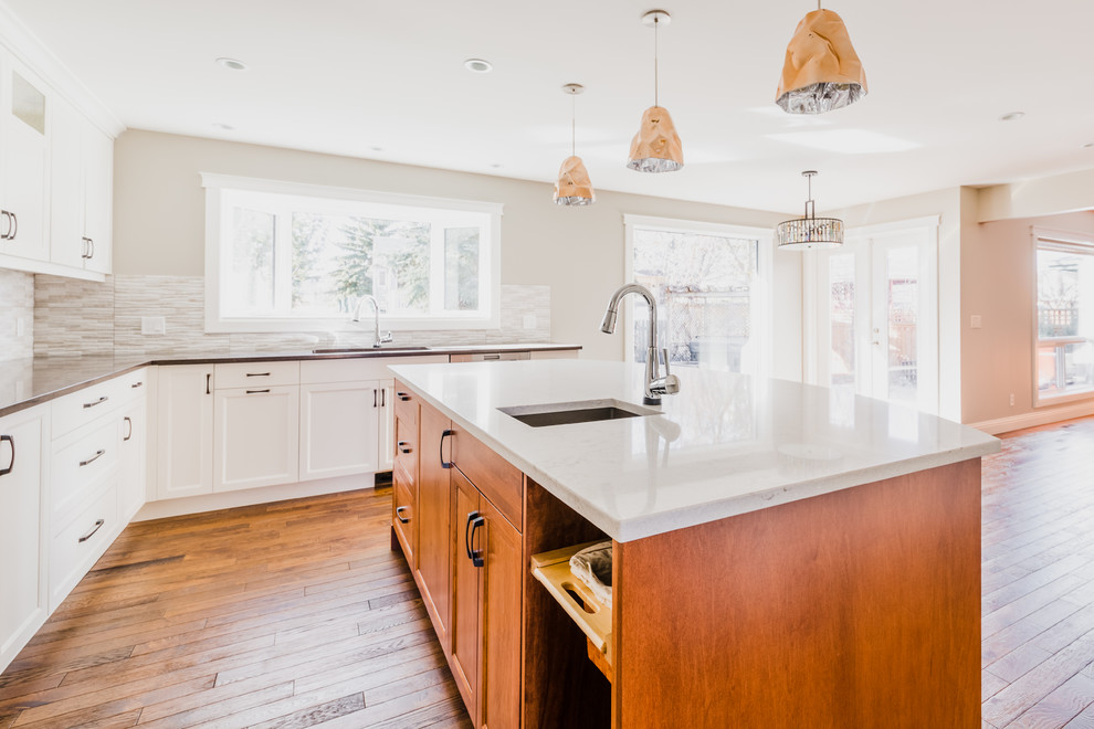 Inspiration for a mid-sized transitional u-shaped medium tone wood floor open concept kitchen remodel in Calgary with an undermount sink, recessed-panel cabinets, white cabinets, quartz countertops, gray backsplash, ceramic backsplash, stainless steel appliances and an island
