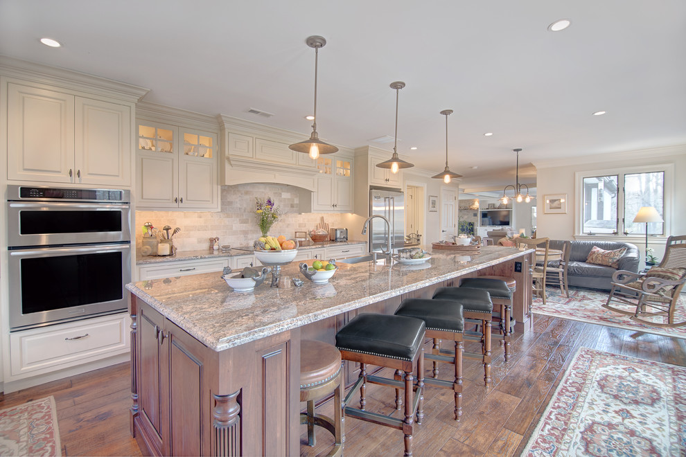 Mid-sized transitional l-shaped kitchen in Baltimore with a farmhouse sink, raised-panel cabinets, white cabinets, granite benchtops, beige splashback, subway tile splashback, stainless steel appliances, medium hardwood floors, with island and brown floor.