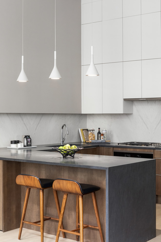 Inspiration for a contemporary u-shaped kitchen in New York with an undermount sink, flat-panel cabinets, white cabinets, grey splashback, light hardwood floors, a peninsula, beige floor and grey benchtop.