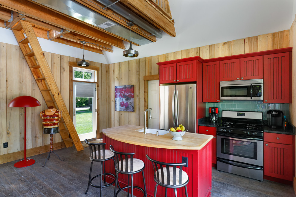 Inspiration for a beach style kitchen in Cincinnati with red cabinets, with island, a farmhouse sink, green splashback, subway tile splashback, stainless steel appliances, dark hardwood floors, brown floor and black benchtop.