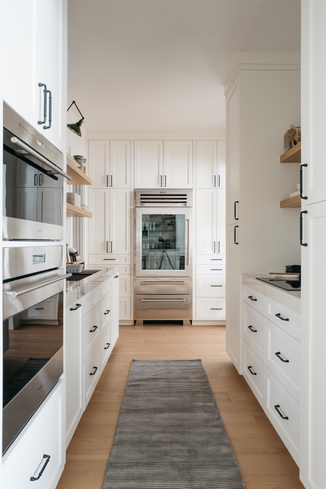 Klassisk inredning av ett stort vit vitt kök, med en rustik diskho, luckor med infälld panel, vita skåp, marmorbänkskiva, vitt stänkskydd, stänkskydd i marmor, rostfria vitvaror, ljust trägolv, en köksö och beiget golv