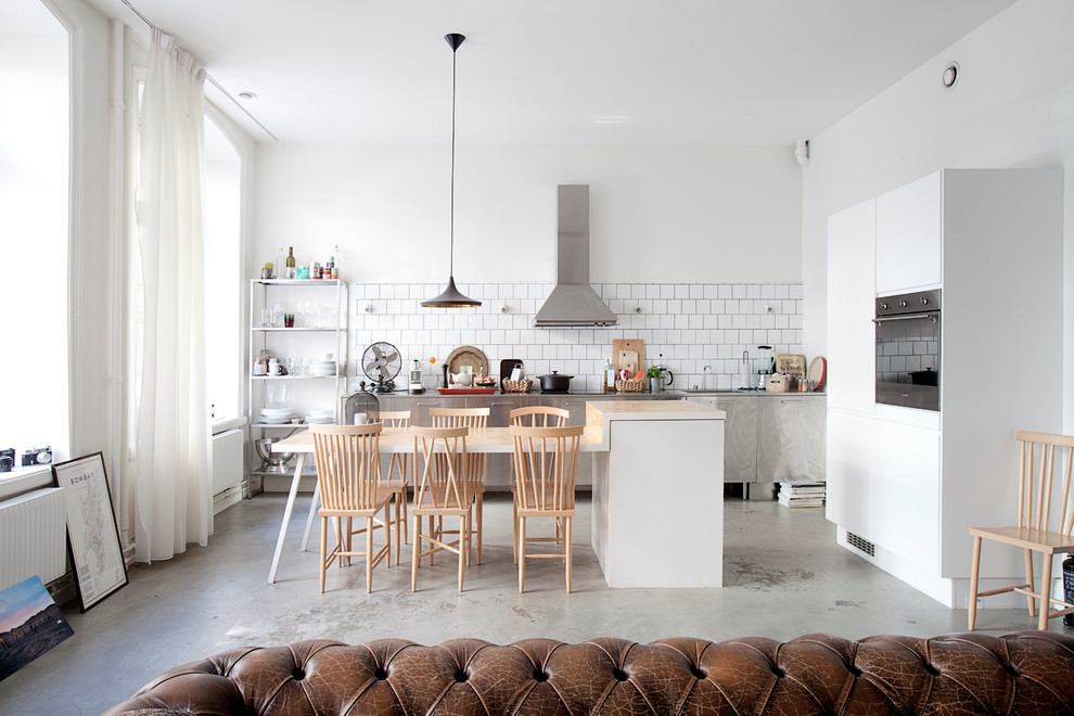 Large scandinavian l-shaped eat-in kitchen in Stockholm with stainless steel cabinets, white splashback, subway tile splashback, with island, a single-bowl sink, stainless steel benchtops and concrete floors.