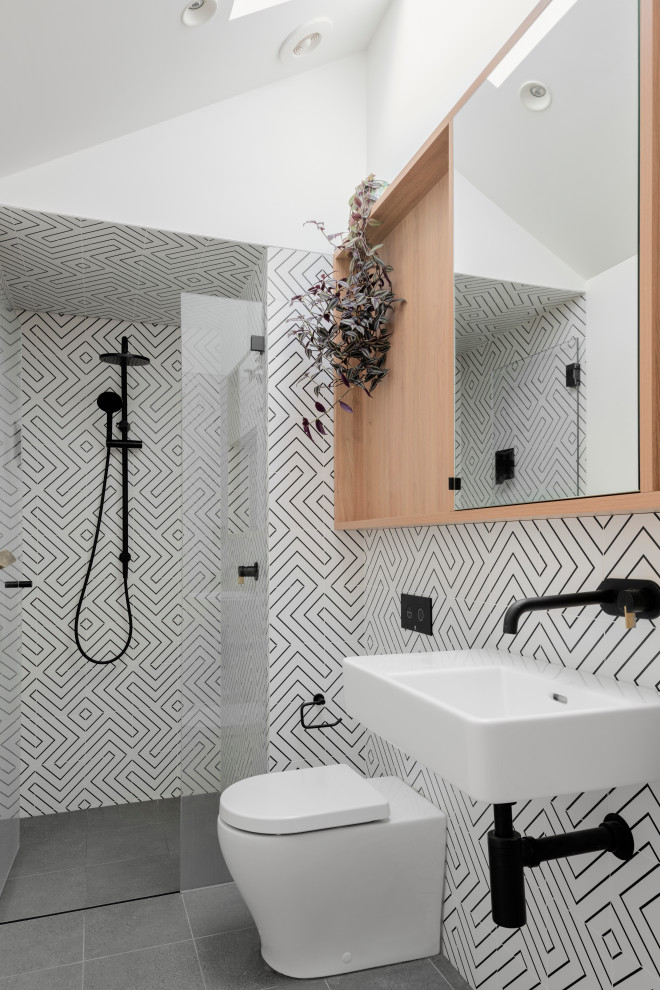 Small contemporary shower room bathroom in Sydney with flat-panel cabinets, medium wood cabinets, an alcove shower, a two-piece toilet, black and white tiles, ceramic tiles, white walls, porcelain flooring, a wall-mounted sink, grey floors, a single sink and a vaulted ceiling.