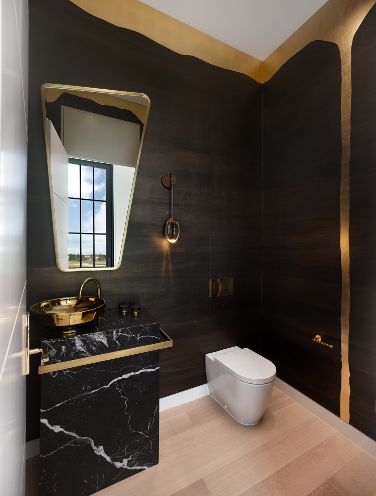 Design ideas for a mid-sized contemporary powder room in Charleston with black cabinets, black walls, light hardwood floors, a vessel sink, marble benchtops, beige floor, black benchtops, a freestanding vanity, wallpaper and wallpaper.