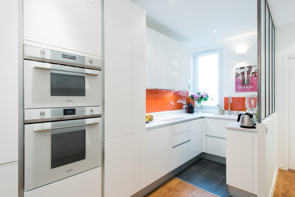 Design ideas for a mid-sized modern u-shaped open plan kitchen in Paris with an integrated sink, beaded inset cabinets, white cabinets, quartzite benchtops, orange splashback, glass tile splashback, panelled appliances and terra-cotta floors.