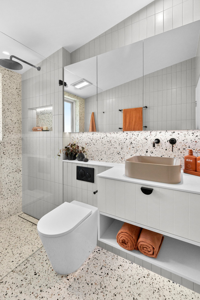 Photo of a medium sized modern grey and black ensuite wet room bathroom in Sydney with flat-panel cabinets, white cabinets, a one-piece toilet, multi-coloured tiles, metro tiles, multi-coloured walls, terrazzo flooring, a vessel sink, solid surface worktops, multi-coloured floors, an open shower, white worktops, a wall niche, a single sink, a built in vanity unit and a vaulted ceiling.