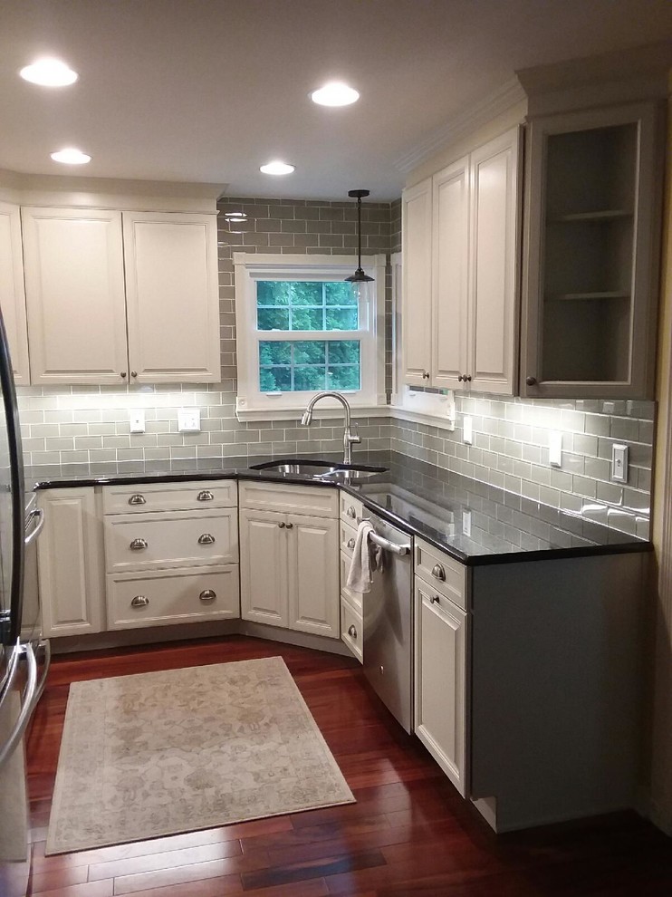 Photo of a small traditional u-shaped eat-in kitchen in Baltimore with an undermount sink, raised-panel cabinets, white cabinets, granite benchtops, grey splashback, ceramic splashback, stainless steel appliances, dark hardwood floors, no island and red floor.
