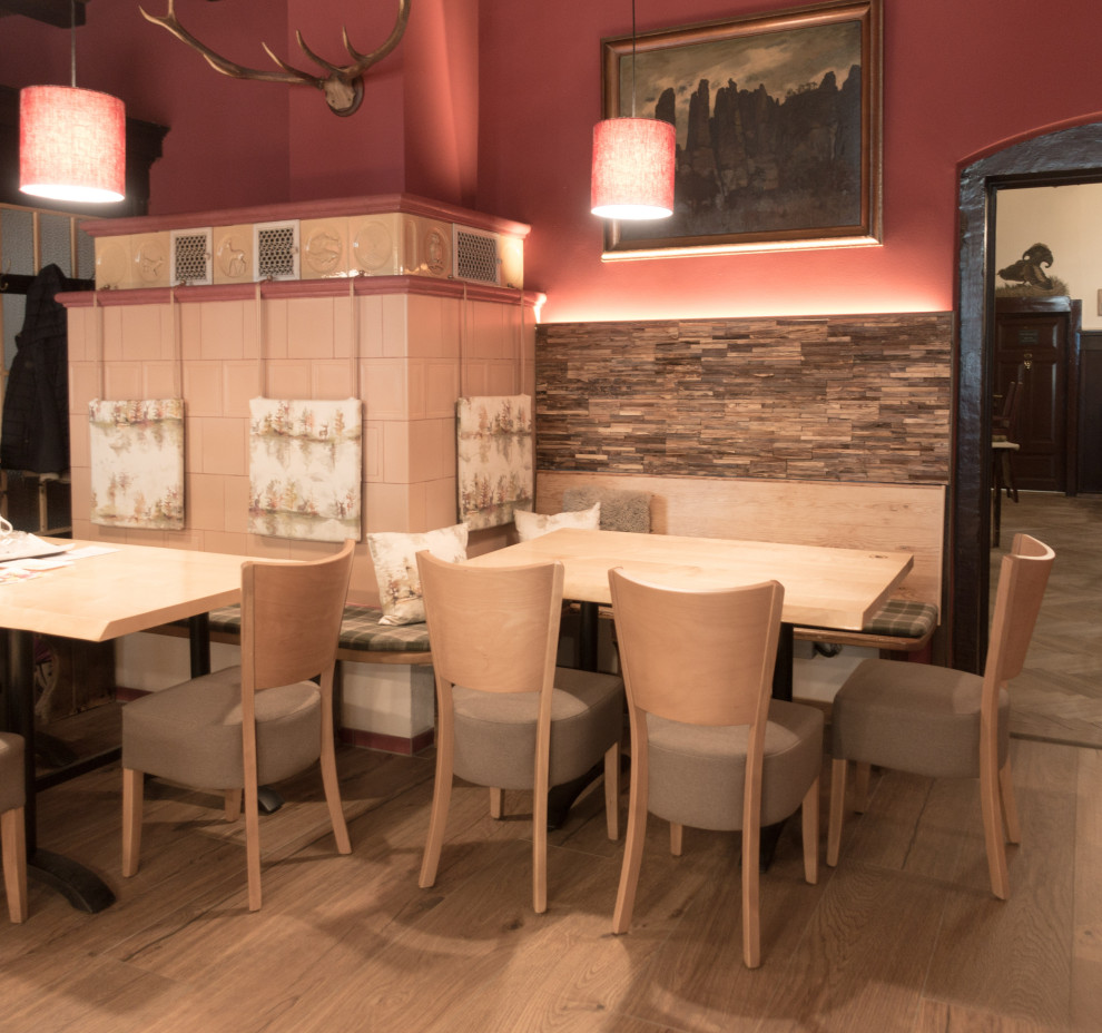 Esempio di una sala da pranzo rustica di medie dimensioni con pareti rosse, pavimento in gres porcellanato, stufa a legna, cornice del camino piastrellata, pavimento marrone, travi a vista e boiserie