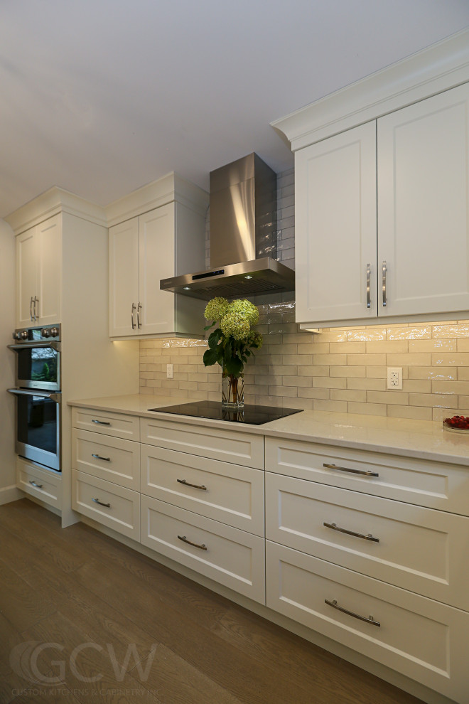 Inspiration for a mid-sized transitional l-shaped eat-in kitchen in Toronto with an undermount sink, shaker cabinets, white cabinets, quartz benchtops, white splashback, ceramic splashback, stainless steel appliances, laminate floors, with island, brown floor and beige benchtop.