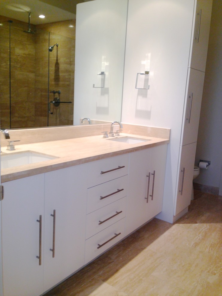 Photo of a mid-sized modern master bathroom in Houston with an undermount sink, flat-panel cabinets, white cabinets, marble benchtops, a drop-in tub, a shower/bathtub combo, a one-piece toilet, beige tile, stone slab, beige walls and travertine floors.