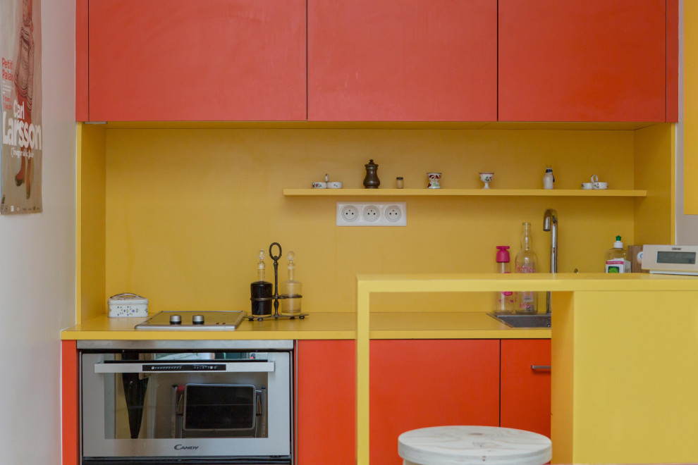 Diseño de cocina actual pequeña abierta con fregadero integrado, armarios con rebordes decorativos, puertas de armario naranjas, encimera de laminado, salpicadero amarillo, salpicadero de pizarra y encimeras amarillas