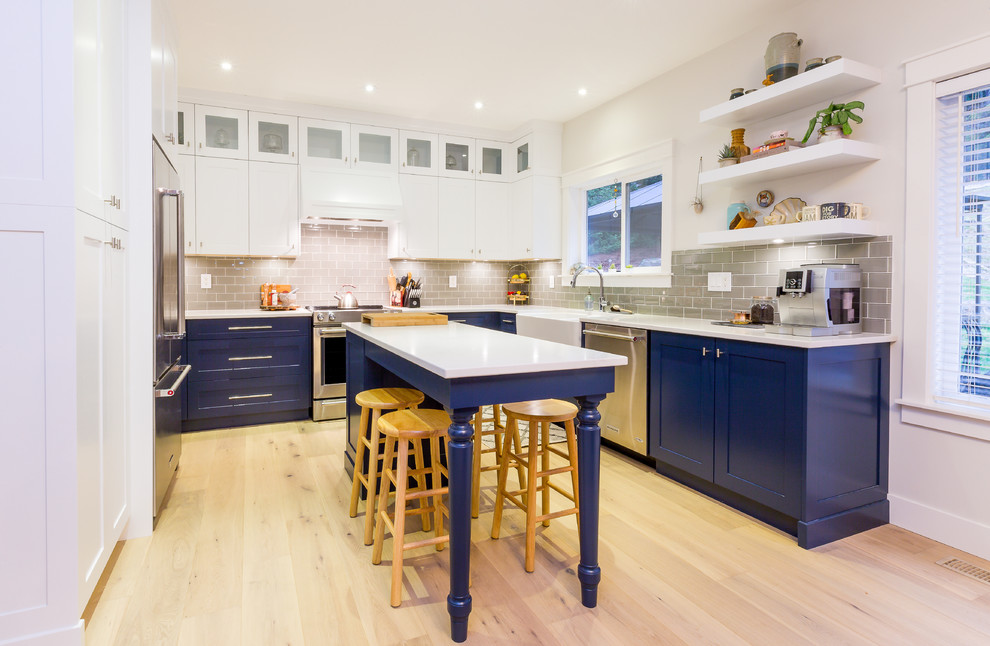 Example of a large transitional u-shaped light wood floor open concept kitchen design with a farmhouse sink, shaker cabinets, blue cabinets, quartz countertops, gray backsplash, glass tile backsplash, stainless steel appliances, an island and white countertops