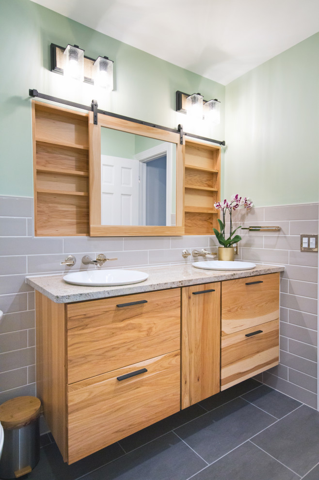 Mid-sized modern bathroom in Other with flat-panel cabinets, light wood cabinets, an alcove tub, a shower/bathtub combo, a two-piece toilet, beige tile, ceramic tile, green walls, porcelain floors, a drop-in sink, granite benchtops, grey floor, a sliding shower screen and beige benchtops.
