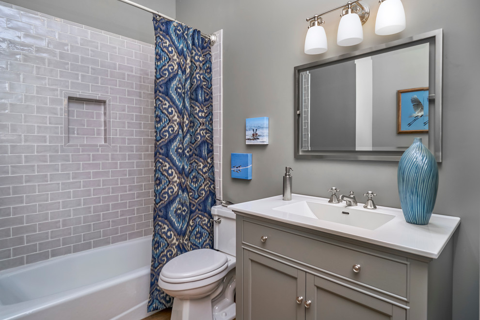 Photo of a mid-sized transitional 3/4 bathroom in Charleston with beaded inset cabinets, grey cabinets, an alcove tub, a shower/bathtub combo, a one-piece toilet, gray tile, subway tile, grey walls, medium hardwood floors, an integrated sink, granite benchtops and white benchtops.