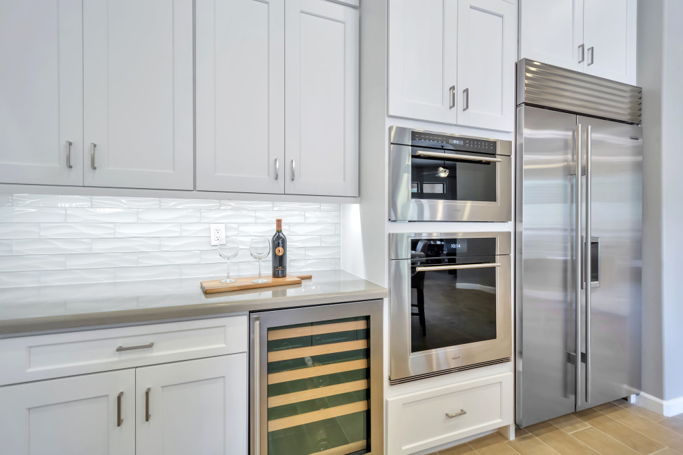 Enclosed kitchen - large transitional u-shaped porcelain tile, beige floor and exposed beam enclosed kitchen idea in Phoenix with a farmhouse sink, shaker cabinets, white cabinets, quartz countertops, white backsplash, glass tile backsplash, stainless steel appliances, an island and white countertops