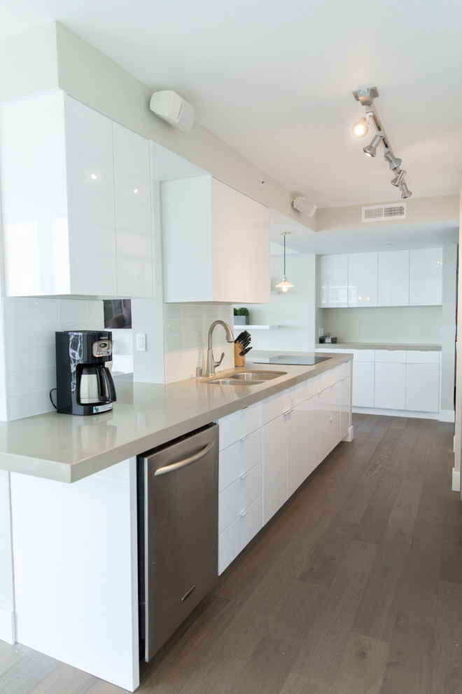 Large modern l-shaped open plan kitchen in San Diego with an undermount sink, flat-panel cabinets, white cabinets, quartz benchtops, white splashback, stainless steel appliances, light hardwood floors, no island, glass tile splashback and brown floor.
