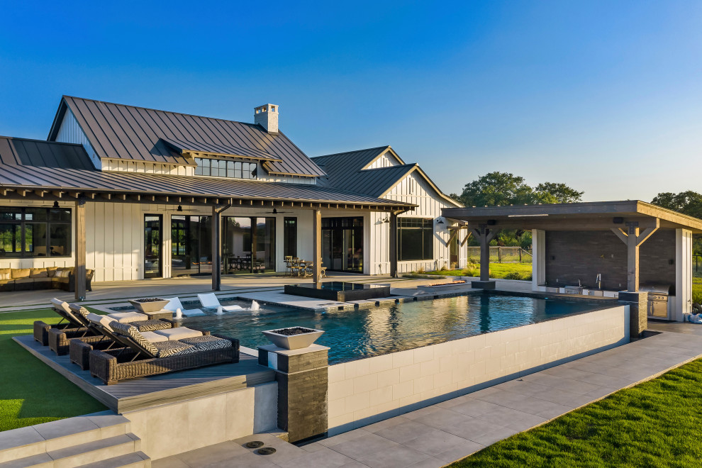 Example of a large farmhouse backyard rectangular infinity pool design with decking