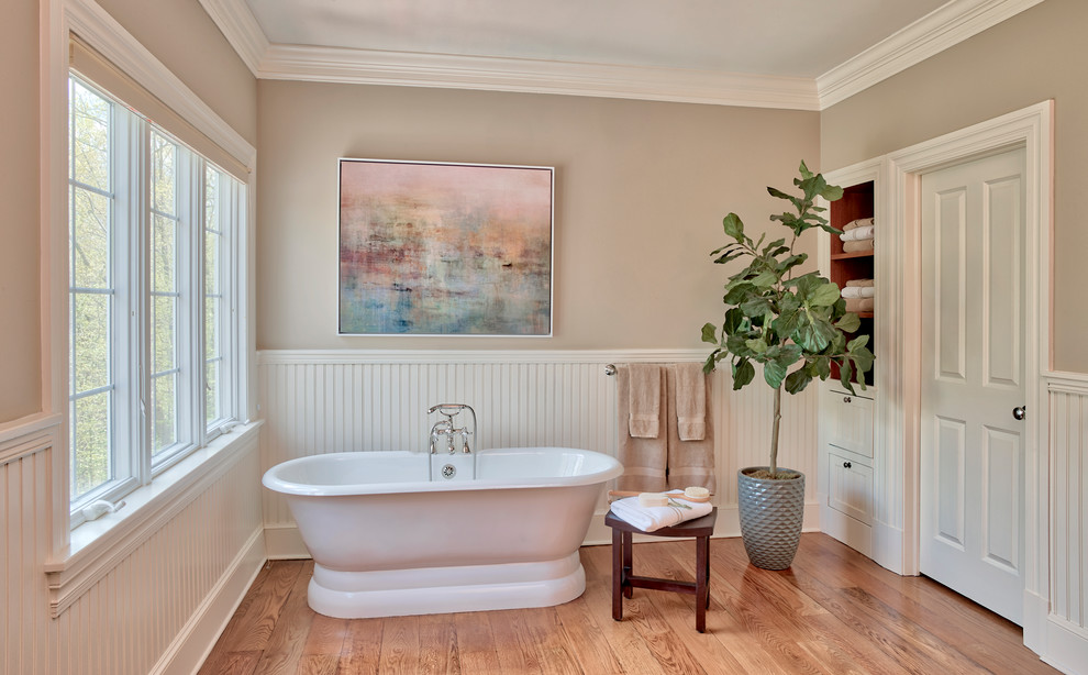 Design ideas for a traditional bathroom in New York with white cabinets, a freestanding tub, beige walls, medium hardwood floors and brown floor.