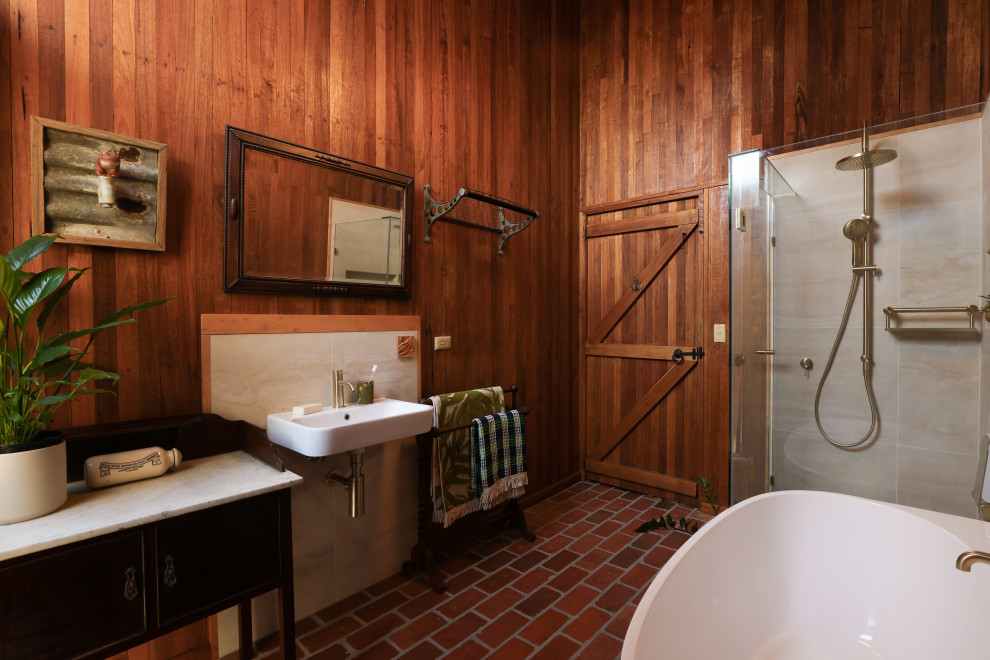Design ideas for a country bathroom in Melbourne with a freestanding tub, a corner shower, beige tile, brown walls, brick floors, a wall-mount sink, red floor, a hinged shower door, a single vanity and wood walls.