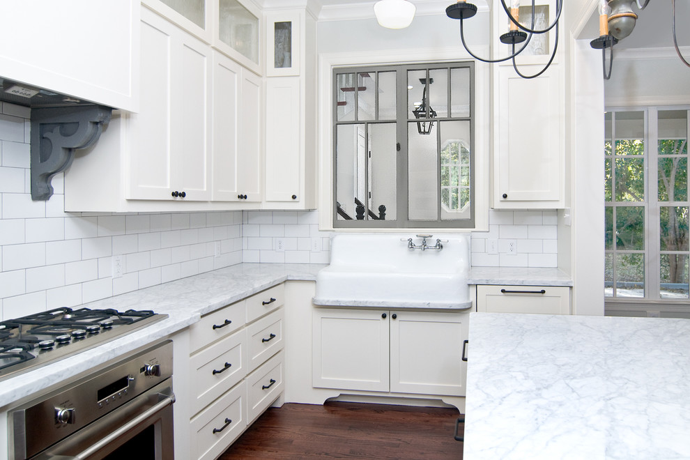 Traditional u-shaped open plan kitchen in Dallas with a farmhouse sink, shaker cabinets, white cabinets, marble benchtops, white splashback, ceramic splashback, stainless steel appliances, dark hardwood floors and with island.