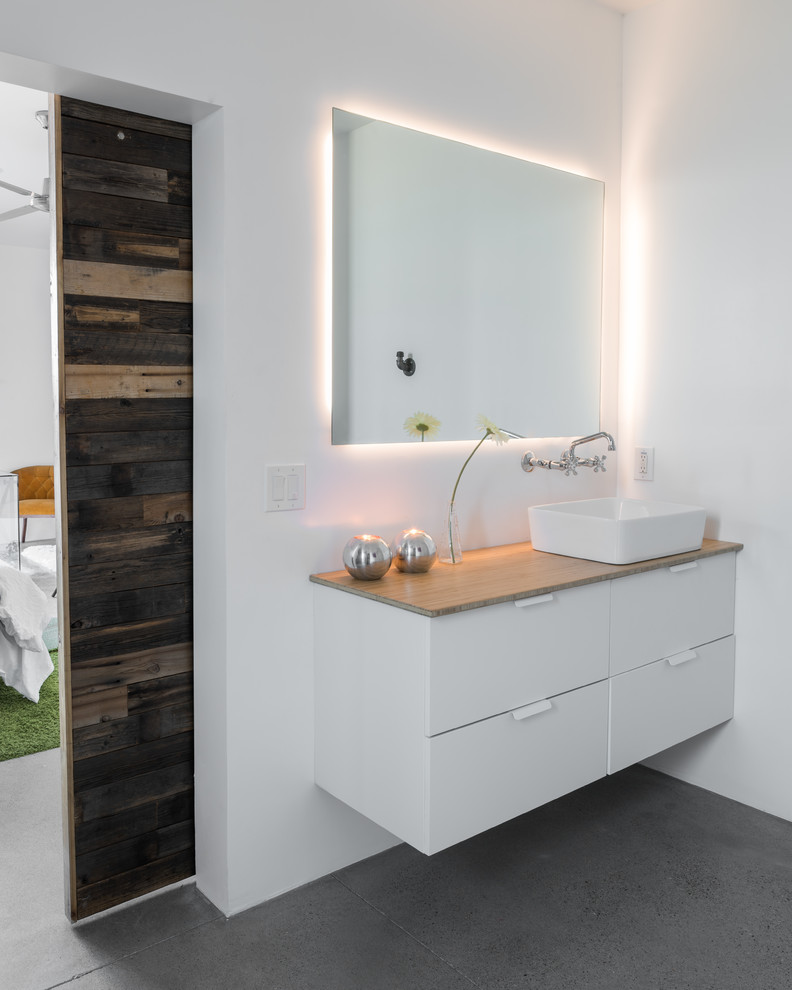 Trendy concrete floor and gray floor bathroom photo in Phoenix with flat-panel cabinets, white cabinets, white walls, a vessel sink, wood countertops and brown countertops