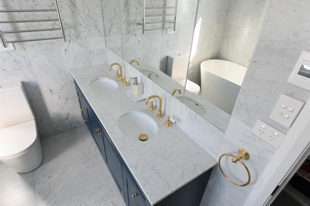 Design ideas for a mid-sized modern master bathroom in Sydney with flat-panel cabinets, white cabinets, a freestanding tub, an open shower, a two-piece toilet, white tile, stone tile, white walls, marble floors, a console sink, marble benchtops, white floor and blue benchtops.
