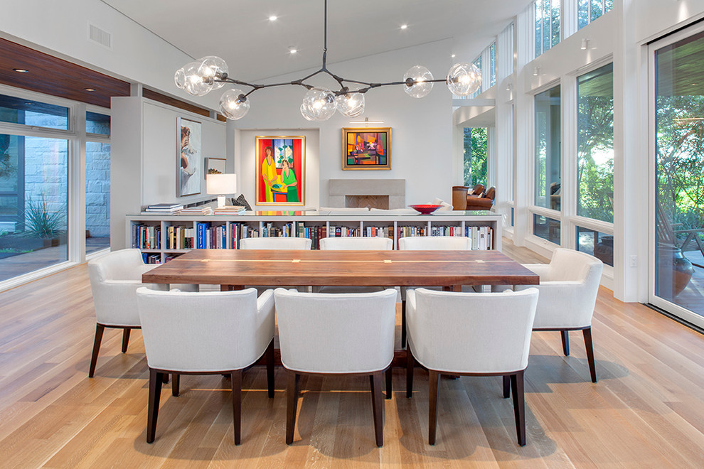 This is an example of a contemporary dining room in Austin with light hardwood floors, a standard fireplace, a stone fireplace surround and white walls.