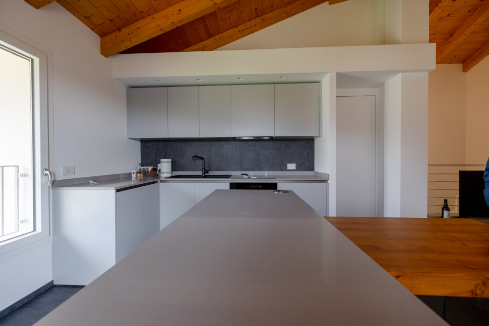 Photo of a mid-sized contemporary l-shaped eat-in kitchen in Milan with a drop-in sink, flat-panel cabinets, grey cabinets, quartz benchtops, black splashback, porcelain splashback, black appliances, porcelain floors, with island, black floor, grey benchtop and exposed beam.